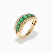 The 14K Yellow Gold Emerald and Diamond Wave Band features a central row of green emeralds bordered by two wavy rows of sparkling white diamonds in an elegant overlapping design.