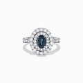 The Platinum GIA Certified Alexandrite and Diamond Double Halo Ring showcases an oval dark blue Alexandrite center stone, two rows of sparkling round diamonds in a double halo, and additional diamonds on the band, all set against a white background.