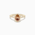 The Espresso 14K Yellow Gold Brown Diamond Halo Ring showcases an oval brown diamond center, encircled by a halo of white diamonds with additional diamonds set along the band.