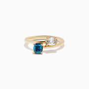 The Bella Bleu 14K Yellow Gold Blue and Light Brown Bypass Diamond Ring showcases an oval white diamond and a cushion-cut deep blue gemstone set side by side on a sleek gold band.