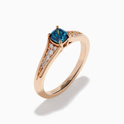 The Bella Bleu 14K Rose Gold Blue and White Diamond Ring showcases a blue rectangular gemstone at the center with small round white diamonds on each side, set against a plain white background.