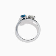 The Bella Bleu 14K White Gold Bypass Ring showcases a blue stone and a light brown diamond set side by side in prongs, displayed against a plain white background.