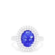 The 14K White Gold Tanzanite and Diamond Ring, 3.13 TCW features a large oval blue tanzanite center stone encircled by two rows of round diamonds in a dazzling halo setting.