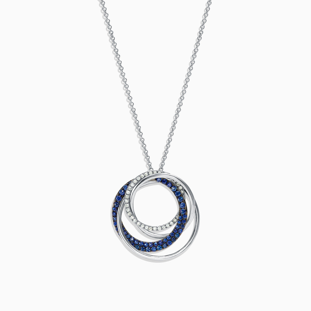 A 14K white gold necklace showcases a pendant of two interlocking circles—one with blue sapphires, the other with diamonds (0.74 TCW)—suspended from a delicate chain on a white background.
