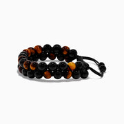 The Mens Tigers Eye Bead Bracelet features alternating glossy black and tiger’s eye brown beads, strung on a black braided adjustable cord. Stylish and versatile, its displayed on a white background—ideal for any occasion.