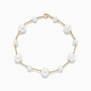 The 14K Yellow Gold Pearl Station Bracelet features round white pearls of varying sizes, evenly spaced along the gold chain, and is displayed on a plain white background.
