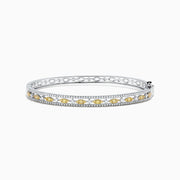 The Canare 14K White Gold Yellow and White Diamond Bangle, 1.27 TCW, features a stunning row of yellow and white diamonds in an intricate center design, elegantly showcased on a white background.