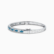 The Bella Bleu 14K White Gold Blue and White Diamond Bangle, 1.27 TCW, features a row of oval blue and white diamonds between two lines of small white crystals, shown on a white background.