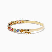 The 14K Yellow Gold Multi Sapphire and Diamond Bangle features a row of multicolored sapphires flanked by diamonds, set across the top against a plain white background.