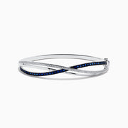 The Royale Bleu 14K White Gold Blue Sapphire and Diamond Crossover Bangle showcases a modern, elegant design with sparkling diamonds and a row of blue sapphires for a sophisticated accessory.