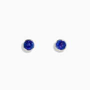 The Nahla Siri Sterling Silver Tanzanite Stud Earrings feature round deep blue tanzanite gemstones in simple sterling silver settings, shown on a white background.