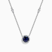 The Royale Bleu 14K White Gold Sapphire and Diamond Necklace, 1.11 TCW, features a round blue sapphire pendant with a halo of clear stones and two diamonds set along each side of the chain.