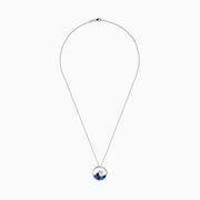 The Seaside 14K White Gold Blue Sapphire and Diamond Wave Pendant is a silver necklace featuring a circular pendant with blue sapphires and diamonds, reflecting the beauty of ocean waves and foam.