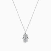 The Novelty 14K White Gold Black and White Diamond Hamsa Pendant features a sparkling eye-design centerpiece on a dainty white gold chain, showcased against a white background.
