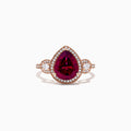 The Bordeaux 14K Rose Gold Rhodolite Garnet and Diamond Ring (3.32 TCW) features a pear-shaped Rhodolite Garnet, diamond halo, and round diamond clusters on each side, all set on a rose gold band.