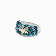 The Seaside Silver and 18K Gold Blue Topaz Starfish Ring, 6.70 TCW, features clusters of oval blue topaz stones set in silver with a gold-outlined starfish accent at the center, shown on a white background.