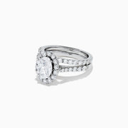 The 14K White Gold Diamond Ring and Matching Band Set, 2.00 TCW, features a large oval center diamond with a halo of round diamonds and a diamond-studded band—displayed against white, ideal for elegant bridal sets.