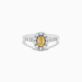 The 14K White Gold White and Fancy Yellow Diamond Ring, 1.10 TCW, features an oval yellow diamond center, haloed by clear round diamonds with more diamonds along the band—a timelessly elegant piece.