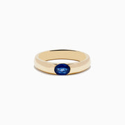 The Mens 14K Yellow Gold Blue Sapphire Ring features a flat band with a round, deep blue sapphire centerpiece, displayed on a plain white background.
