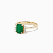 The Brasilica 14K Yellow Gold Emerald and Diamond Ring (1.57 TCW) showcases a rectangular emerald center, accented by round white diamonds on each side, set against a white background.