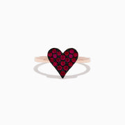 The 14K Rose Gold Ruby Heart Ring showcases a heart-shaped centerpiece with red gemstones, casting a gentle shadow on a white background.