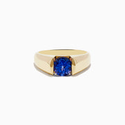 The Nahla Siri 14K Yellow Gold Tanzanite Ring features a wide band and a single round blue gemstone at the center, displayed on a white background.
