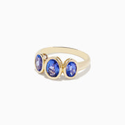The Nahla Siri 14K Yellow Gold Tanzanite Three Stone Ring features three oval blue tanzanites in bezel settings on a simple gold band.