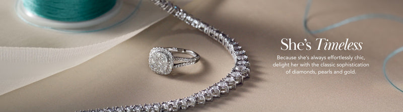 A diamond ring and tennis bracelet are displayed next to a spool of teal ribbon. The text reads: Shes Timeless. Because shes always effortlessly chic, delight her with the classic sophistication of diamonds, pearls and gold.