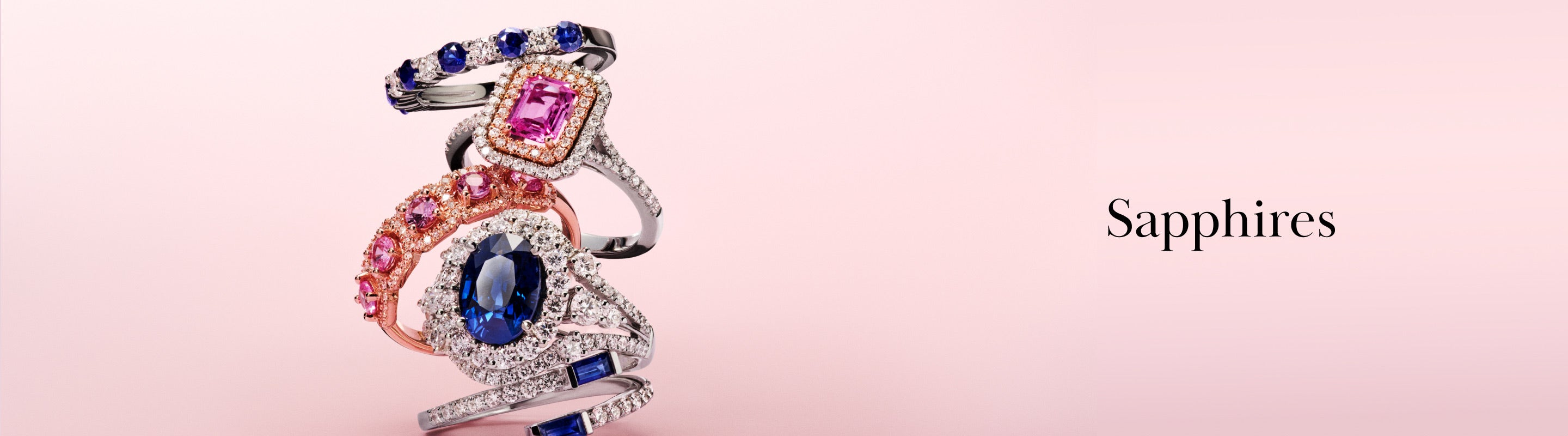 Three ornate sapphire rings with blue, pink, and multicolored gemstones are stacked on a pink background. The word Sapphires appears to the right in elegant black text.