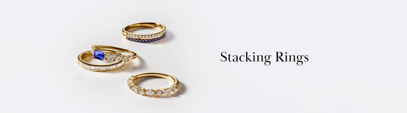 Four gold stacking rings with various gemstones and diamond accents are arranged on a white surface next to the words Stacking Rings in elegant black text.