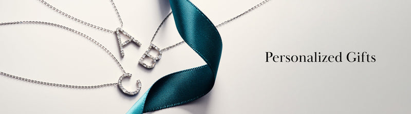 Three silver necklaces with letter pendants A, B, and C lay on a pale surface beside a teal ribbon, with the text Personalized Gifts written on the right.