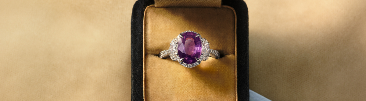 A gold ring with a large green gemstone surrounded by diamonds rests on a silky teal fabric. The text Exotic Gems appears on the left side.