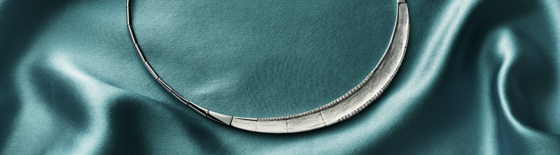 Three shiny silver rings, including a heart, a starburst design, and a textured band, rest on rippling water with a soft blue background. The word Silver appears on the right.