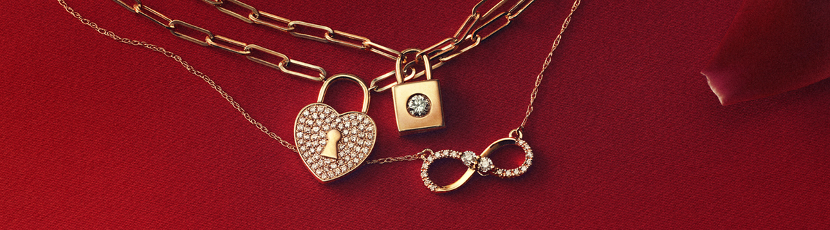 Gold necklaces with diamond-accented heart lock, square lock, and infinity symbols on a red background.