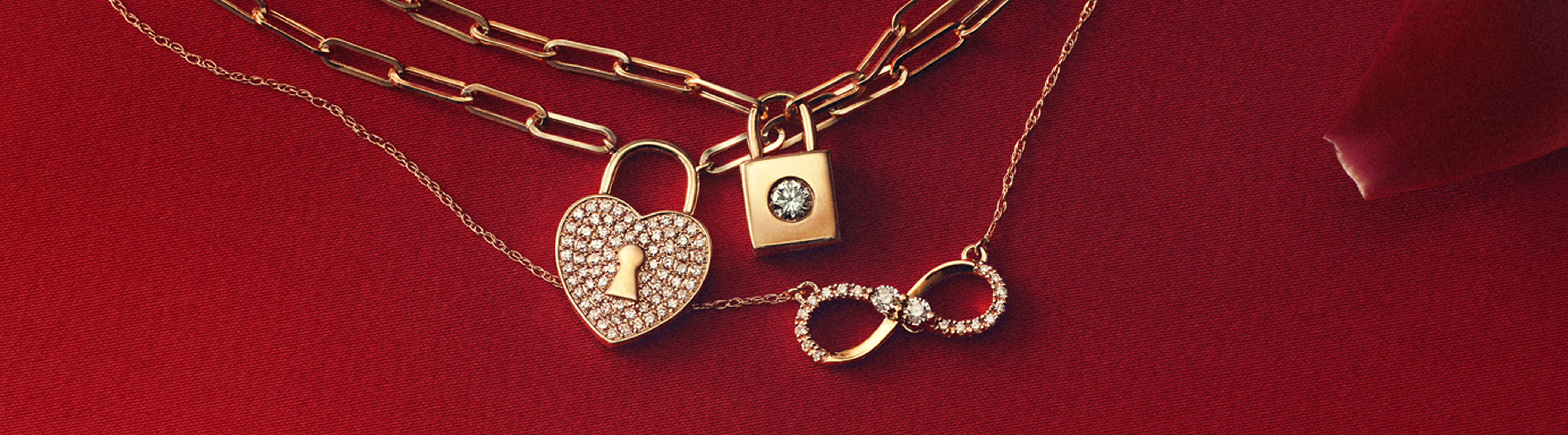 Gold necklaces with diamond-accented heart lock, square lock, and infinity symbols on a red background.