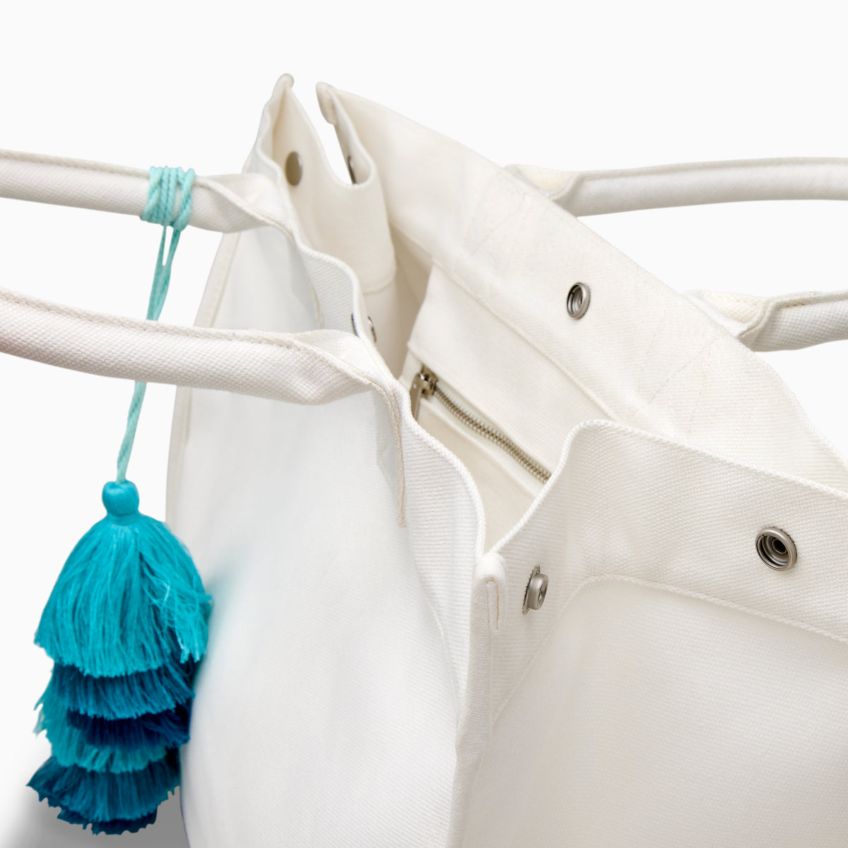 The Beach Bag - White is a large canvas tote with two handles, featuring blue and turquoise tassels and EAFY printed in black near the bottom right corner.