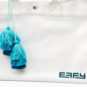 The Beach Bag - White is a large canvas tote with two handles, featuring blue and turquoise tassels and EAFY printed in black near the bottom right corner.