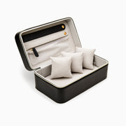 The Jewelry Vegan Leather Travel Box - Black is a rectangular, zippered box with a light interior, three beige pillows, a pocket with zipper and two gold buttons. Dimensions: 8 L x 5 W x 3 H.