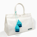 The Beach Bag - White is a large canvas tote with two handles, featuring blue and turquoise tassels and EAFY printed in black near the bottom right corner.