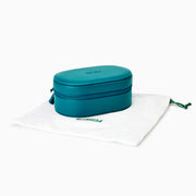 The Effy Oval Travel Case is a small, oval-shaped zippered case in teal vegan leather with a matching teal zipper, closed and displayed on a white background.