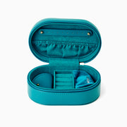 The Effy Oval Travel Case is a small, oval-shaped zippered case in teal vegan leather with a matching teal zipper, closed and displayed on a white background.