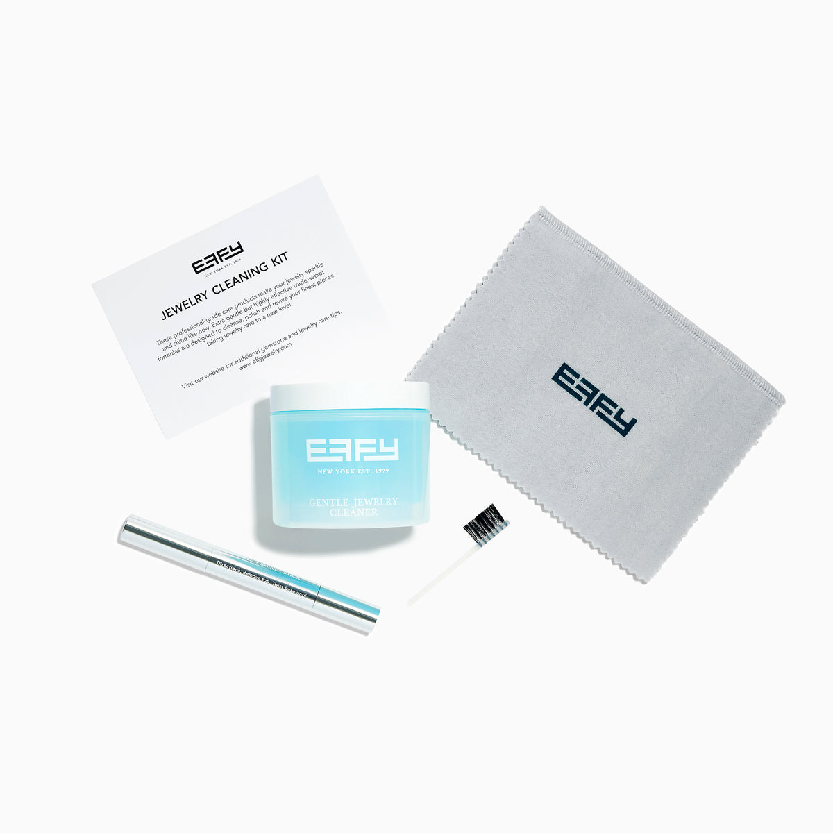 The Jewelry Cleaning Kit, featuring a Crystal Repair Cleanser jar, dual-ended brush, pen-style Jewelry Cleaner, and gray EEFY Polishing Cloth, is neatly displayed on a white background for Sparkle + Shine.