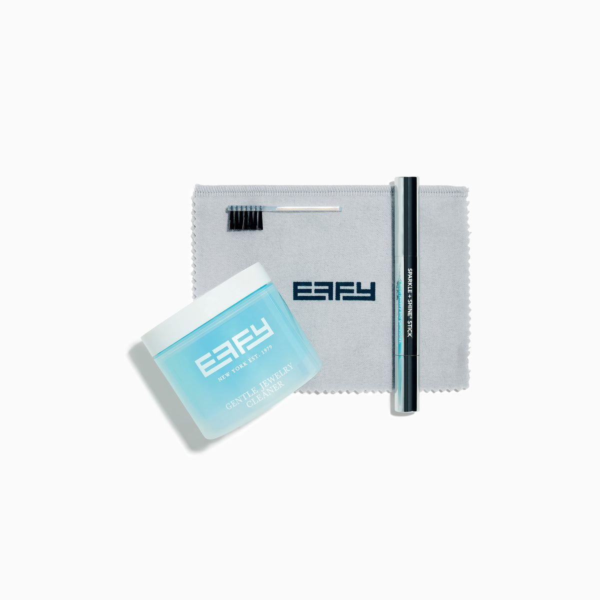 The Jewelry Cleaning Kit, featuring a Crystal Repair Cleanser jar, dual-ended brush, pen-style Jewelry Cleaner, and gray EEFY Polishing Cloth, is neatly displayed on a white background for Sparkle + Shine.