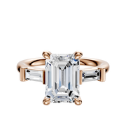 The 14K Rose Gold 3-Stone Baguette East/West Side Stones 0.125TCW Engagement Ring features a central stone accented by tapered baguette side stones, shown on a plain white background.