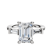 The 14K White Gold 3-Stone Baguette East/West Side Stones 0.125TCW Engagement Ring features a center stone flanked by baguette-cut side stones in a classic prong setting, displayed against a white background.