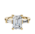 The 18K Yellow Gold 3-Stone Baguette East/West Side Stones 0.125TCW Engagement Ring features a large emerald-cut center stone with two smaller baguette-cut side stones in a classic four-prong setting.