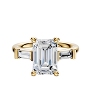 The 18K Yellow Gold 3-Stone Baguette East/West Side Stones 0.125TCW Engagement Ring features a large emerald-cut center stone with two smaller baguette-cut side stones in a classic four-prong setting.