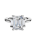 An 18K white gold engagement ring featuring a three-stone design with 0.125 TCW baguette side stones set north/south, showcased on a simple, elegant band against a plain white background.