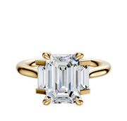A 14K yellow gold engagement ring with a north/south set, featuring a main stone and baguette side stones (0.125TCW), displayed against a plain, light background.