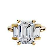 The 18K Yellow Gold 3-Stone Baguette Side Stones Set North/South 0.25TCW Engagement Ring showcases a large center diamond with baguette-cut side stones on a clean, plain background.